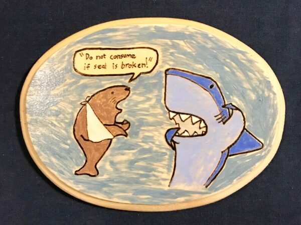 Wooden plaque with a shark and an injured seal on it. Contains the words "Don't consume if seal is broken."