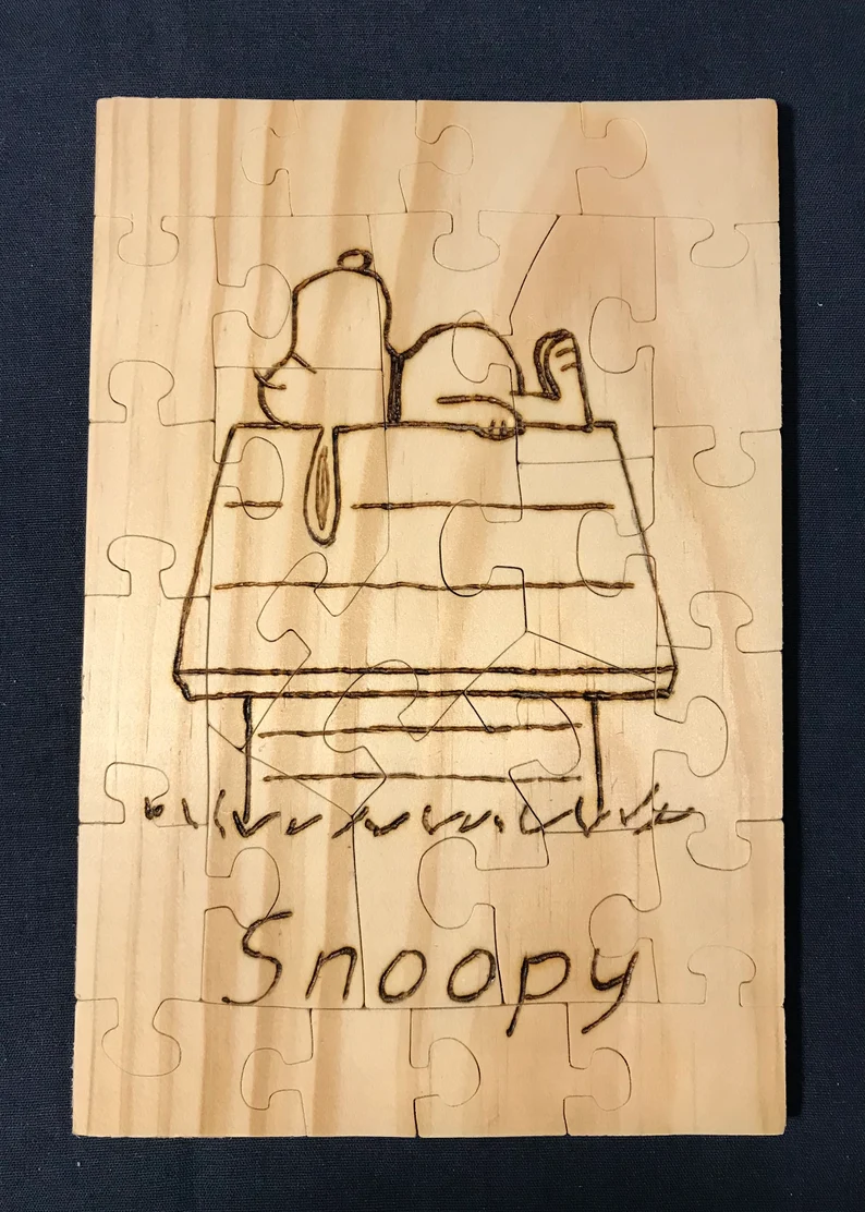 Wooden puzzle of a wood burned Snoopy on his doghouse