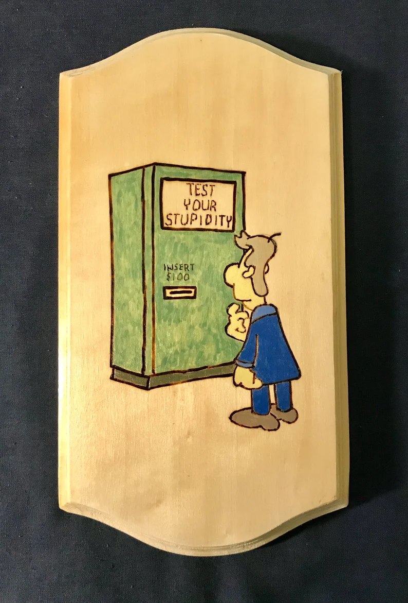 plaque with a picture of a man standing at a vending machine that reads "test your stupidity"